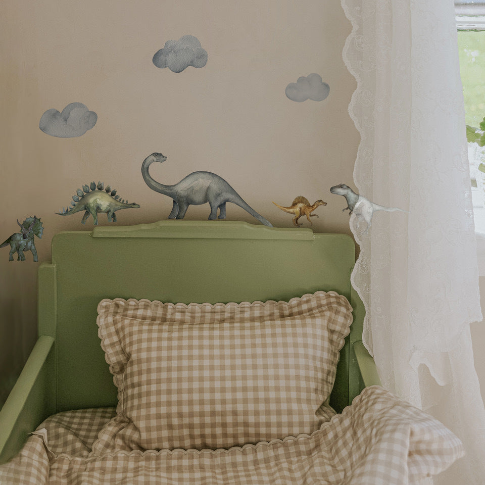 Dinosaur wall decals with clouds over them, lined up on a bed