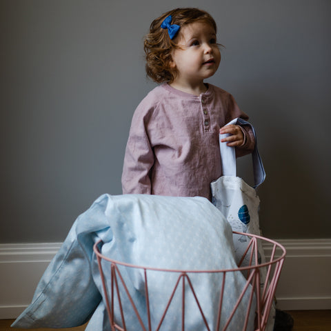 Child standing next gooselings duvet that is placed in a basket