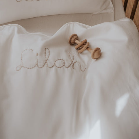 Baby Duvet in White Color, with the name Lilah written on it in beige with a rattle on top of it