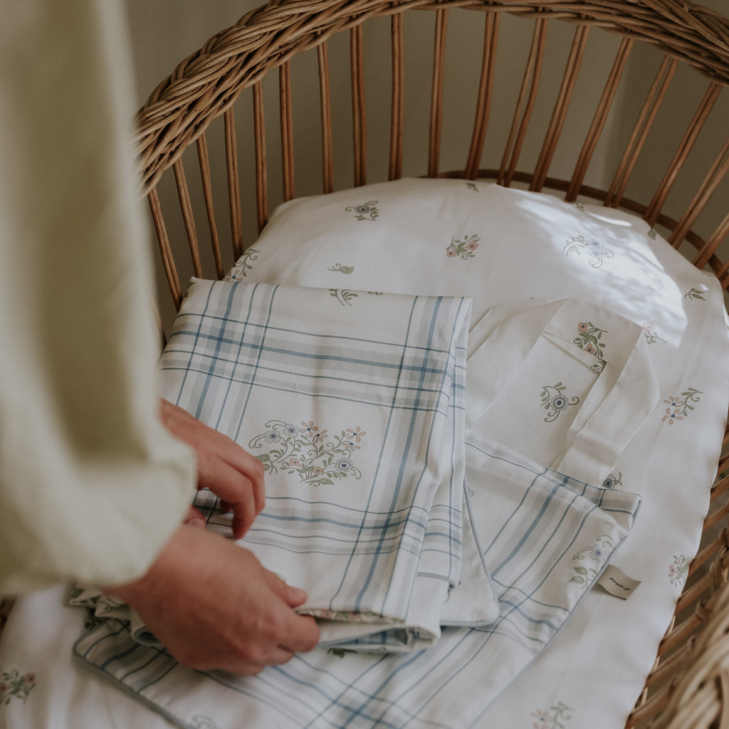 A mother folding sheets on top of the Fleur and Stripe Print Crib Sheet in Multi Color