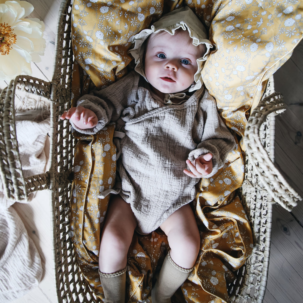 Baby laying in a moses basket on top of the baby duvet in "Bird's Song" print in the color mustard