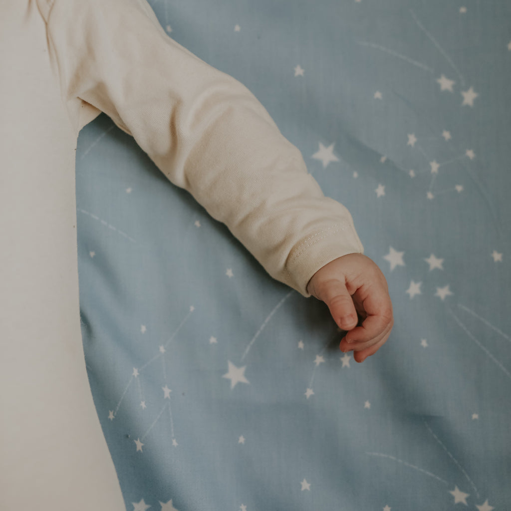 Baby's hand laying on top of crib sheet in the Once Upon A Time print in color blue