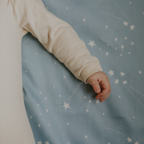 Baby's hand laying on top of crib sheet in the Once Upon A Time print in color blue