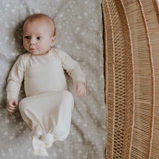 Baby laying on top of "Bird's Song" printed crib sheet in the color grey