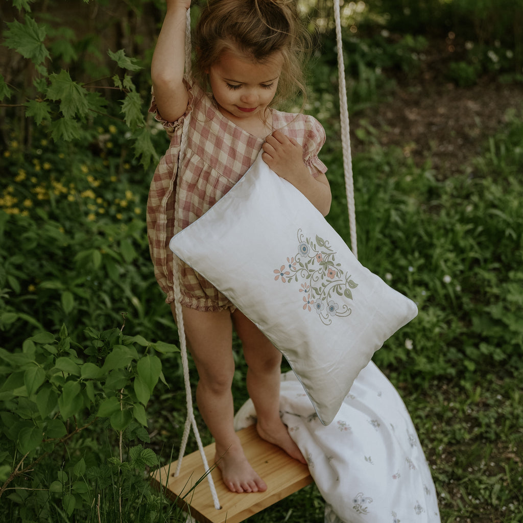Toddler holding the toddler pillow on a swing in the Fleur and Stripe print in multi color